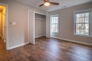 Empty room with wooden parquet flooring, white trim, ceiling fan, and natural light from windows.
