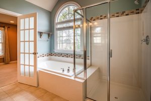 Modern bathroom with a white ceramic bathtub, glass shower, and large arched window.