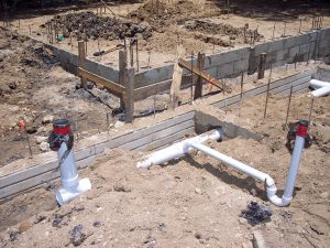 Cement foundation at a construction site with exposed plumbing pipes in the ground.