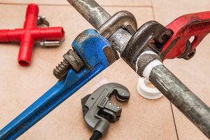 Plumbing pipe wrenches and metal pipes arranged on a surface, symbolizing plumbing work.