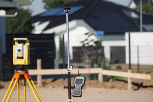 Surveying equipment set up at a construction site with buildings visible in the background.