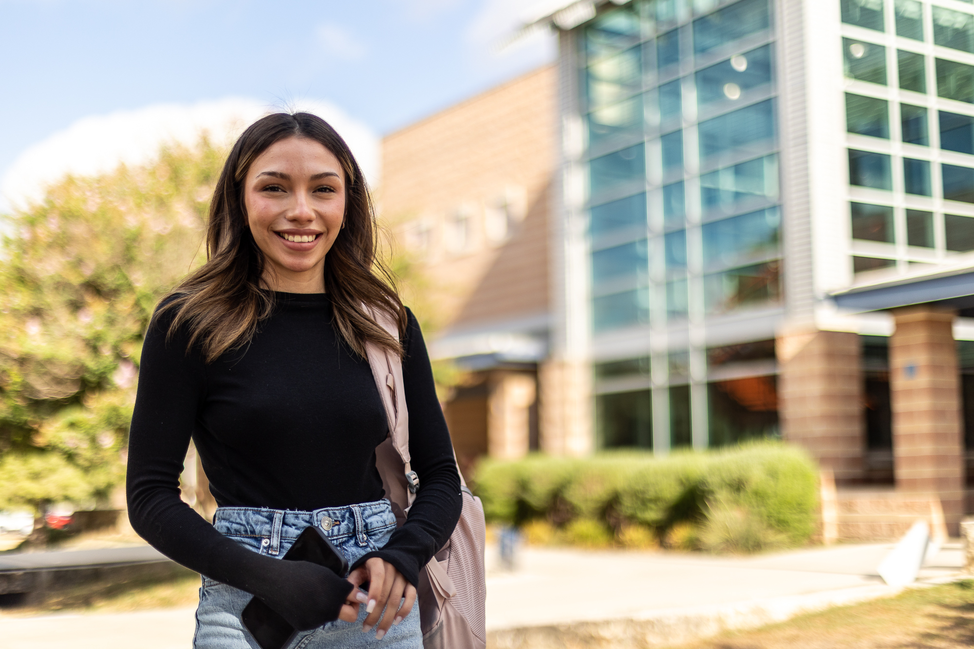 Young woman with a shoulder bag stands outside of a classroom building.