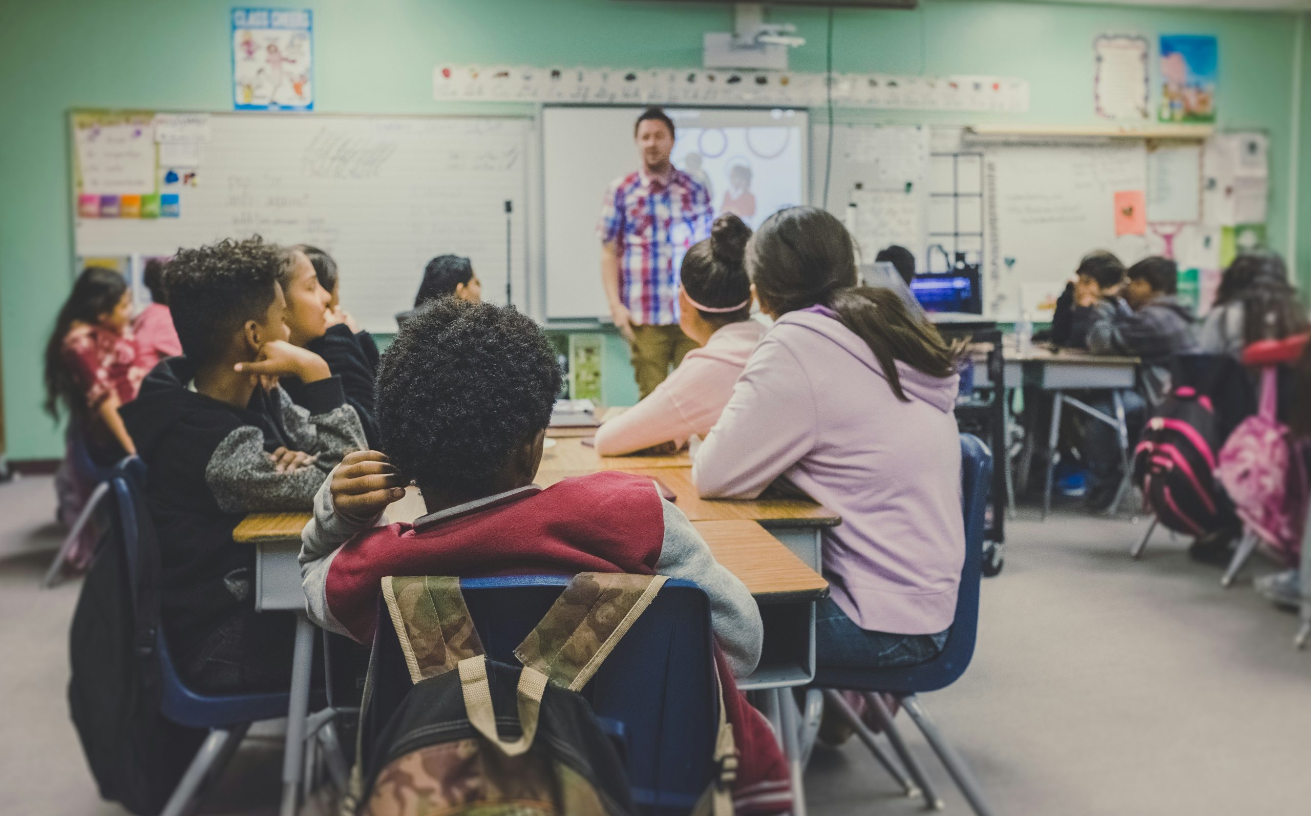 Man stands in front of a classroom populated by adolescent students.